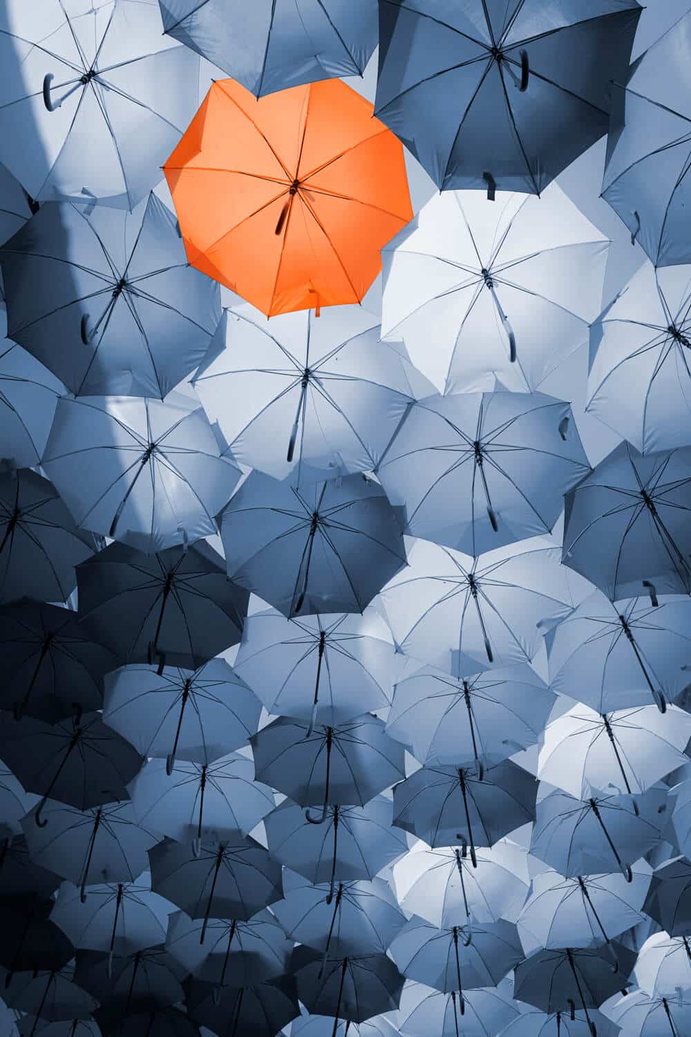 one orange umbrella amongst grey umbrellas